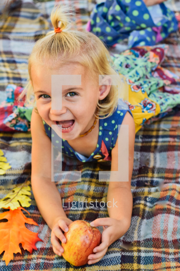 happy toddler girl on a plaid blanket holding an apple 