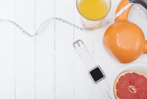 grapefruit, measuring tape, orange juice, kettle ball weight, and smartwatch fitness tracker on a white background 