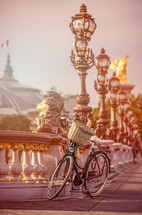 bicycle with a basket parked by railings and ornate street lamps in Paris 