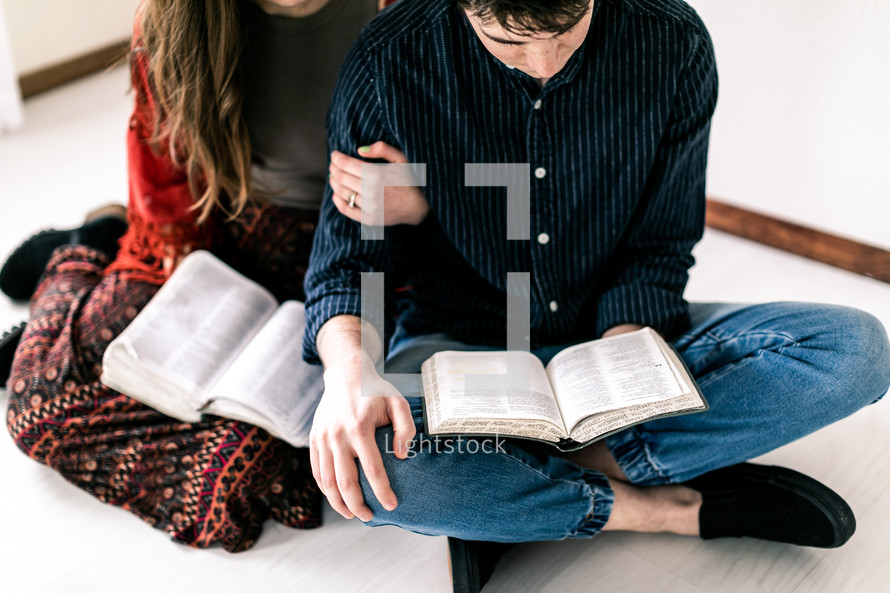 a couple sitting on the floor reading Bibles 