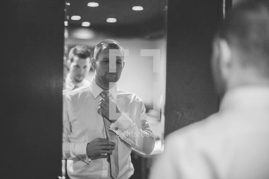 Two men standing in front of a mirror putting on ties.