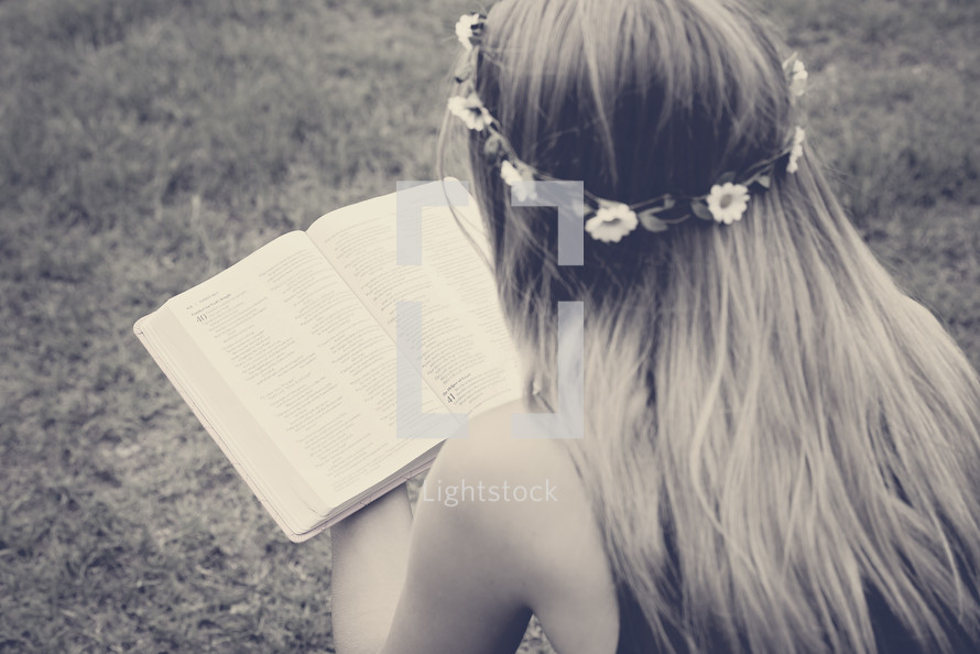 a girl with flowers in her hair reading a Bible 