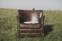 an open Bible in a leather chair in a field 