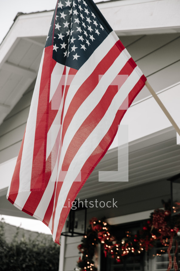 An American flag hanging above a front porch decorated for Christmas.