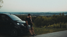a couple leaning against their parked van looking out at mountain views 