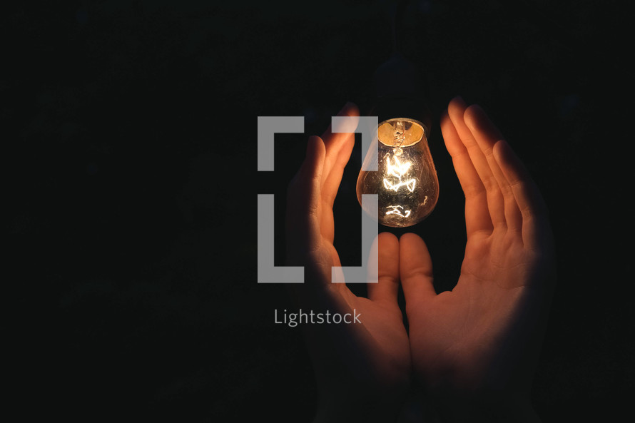 illuminated hands surrounding a light bulb