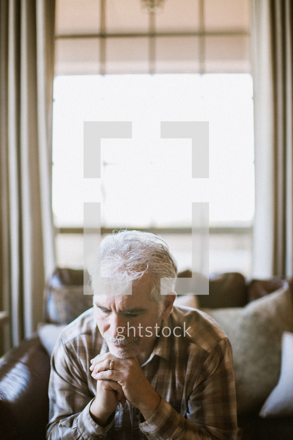 elderly man sitting on a couch praying