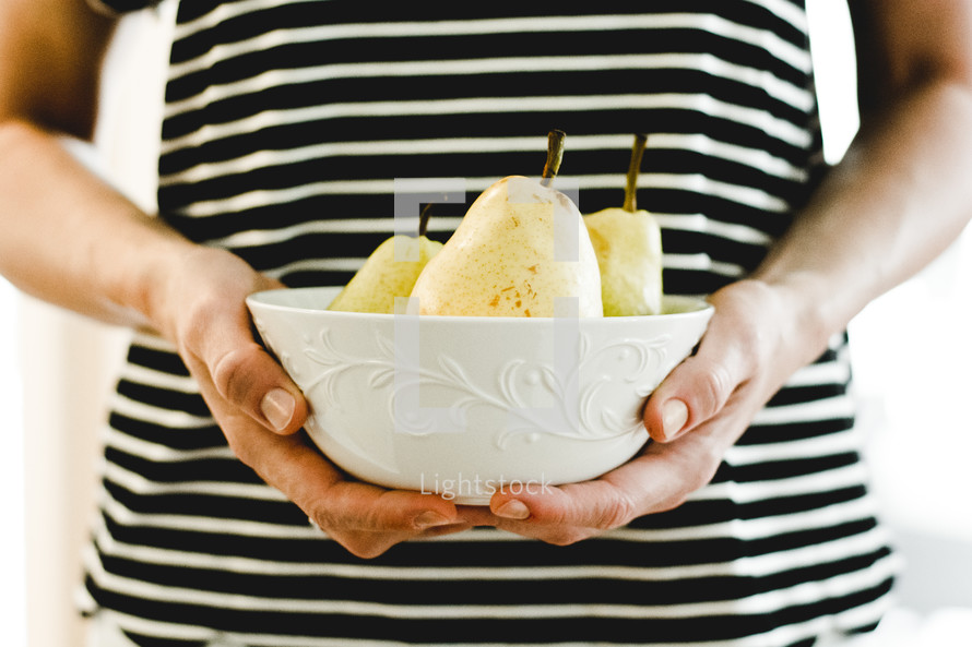 a woman holding a bowl of pears 
