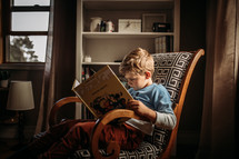a little boy sitting in a chair reading a book 