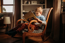 a boy sitting in a chair reading a book 