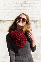 woman smiling outdoors in a scarf and sunglasses 