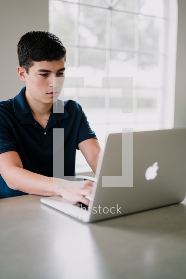 a teen boy sitting in front of a laptop computer 