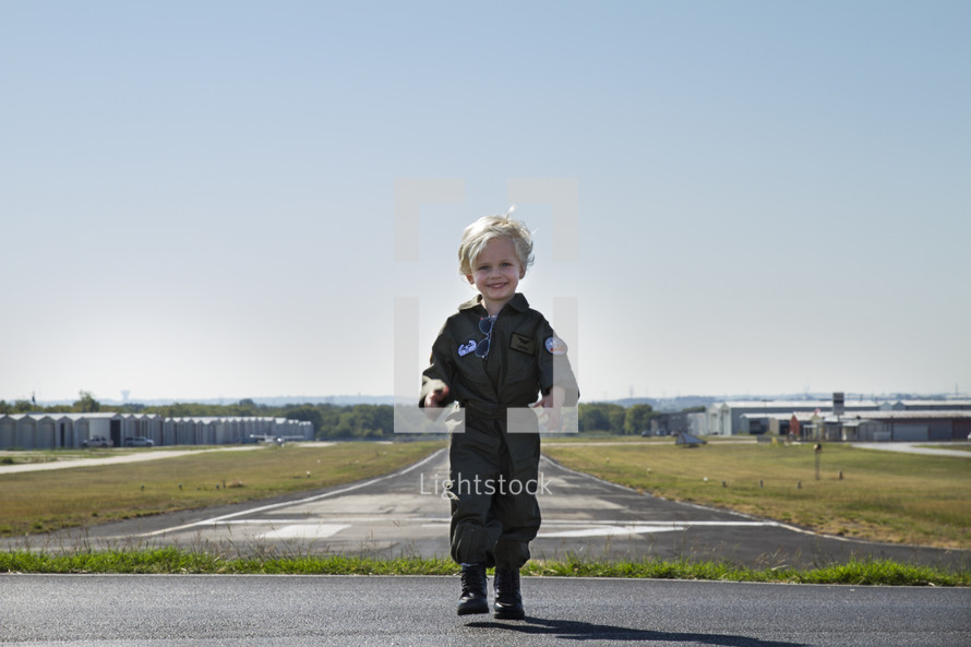 a boy child in a pilot uniform standing in front of a runway
