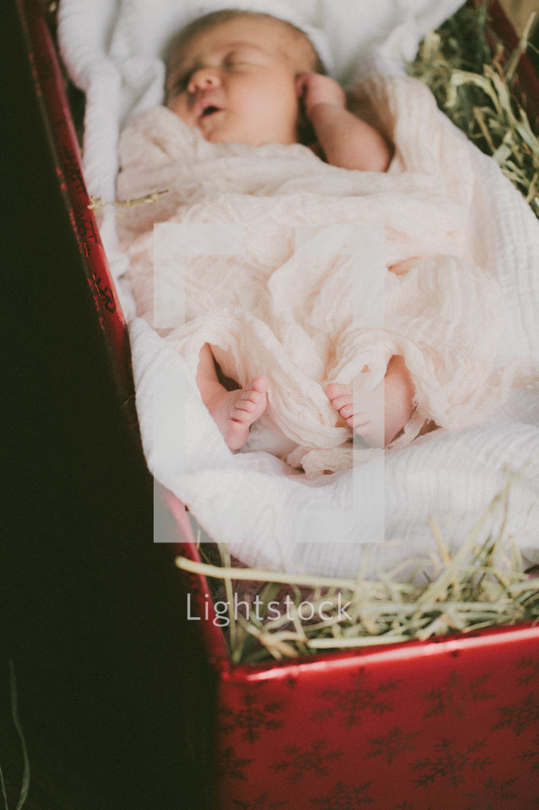 A baby lying in a Christmas present full of hay