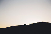 silhouette of a distant couple standing on a hill holding hands
