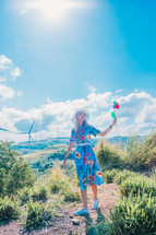 a woman holding pinwheels standing near wind turbines 