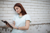 a young woman reading a Bible standing in front of a white wall 