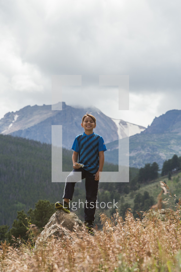 a young boy standing outdoors in front of a mountain peak 