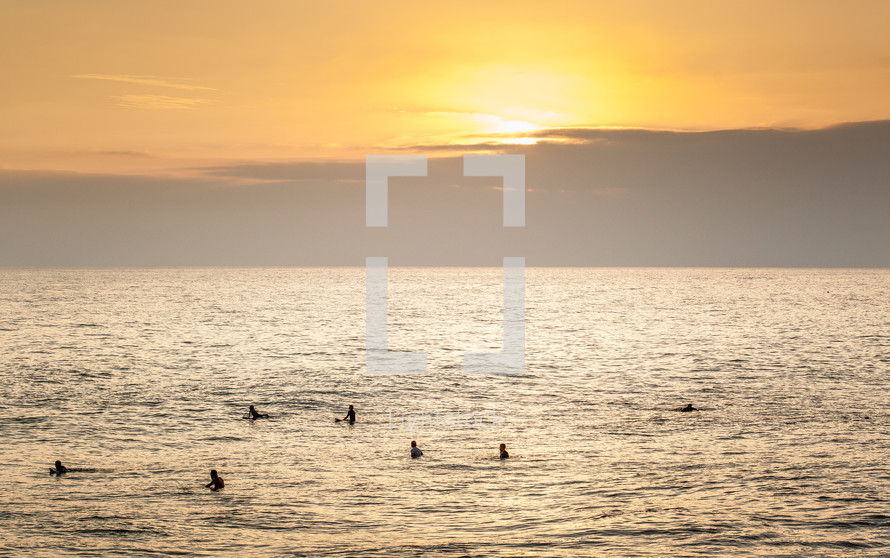 surfers in the water at sunset 
