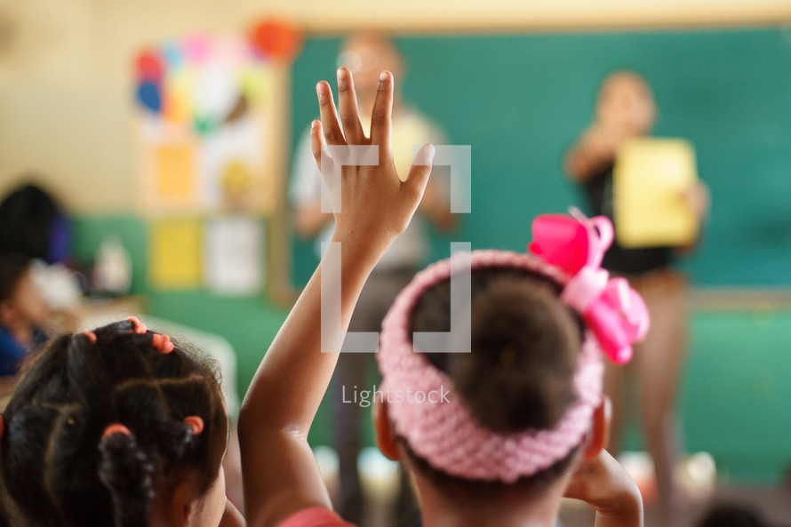 a child with her hand raised in a classroom 