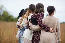 group of women walking through a field holding Bibles 