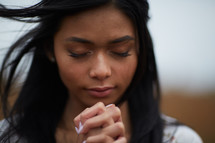 face of a  young woman standing in a field praying 