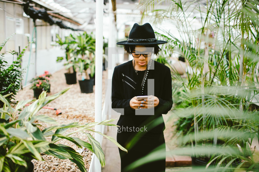 An African American woman in a black hat texting in a green house 