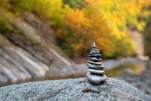 Balanced stones on blurred mountain background in warm, sunset light with autumn foliage.