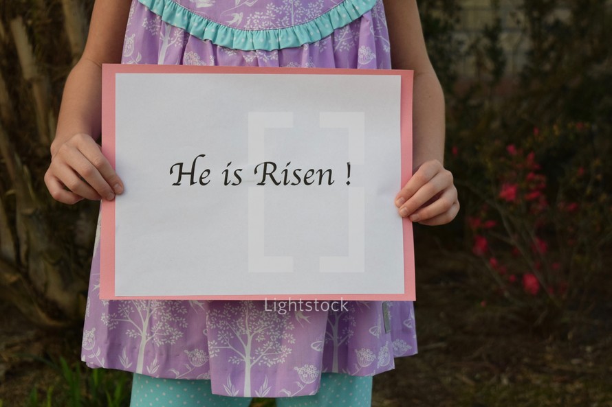A little girl holding a He is Risen sign 