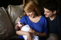 Smiling couple sitting on a sofa holding an infant.