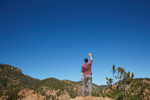 a man standing on a mountain with hand raised 