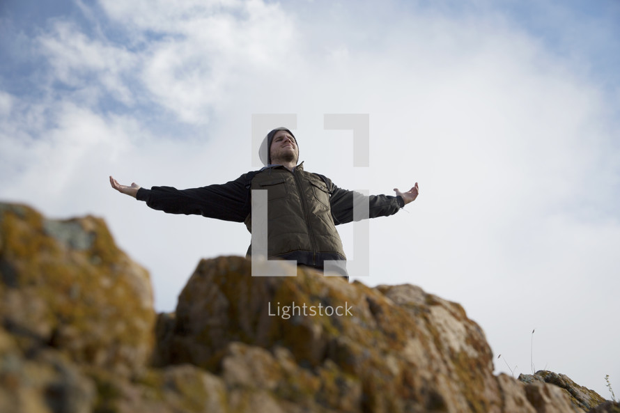 man standing on a mountainside with raised arms 