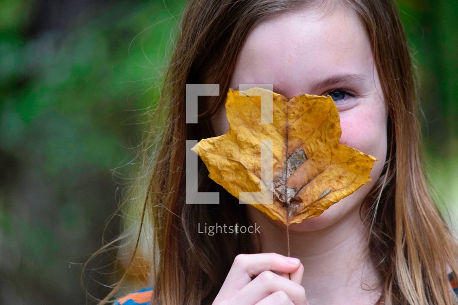 a girl hiding behind a fall leaf 
