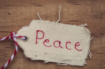 A Christmas gift tag labeled "Peace", against a wood grain background.
