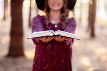A woman standing in the woods with an open Bible 