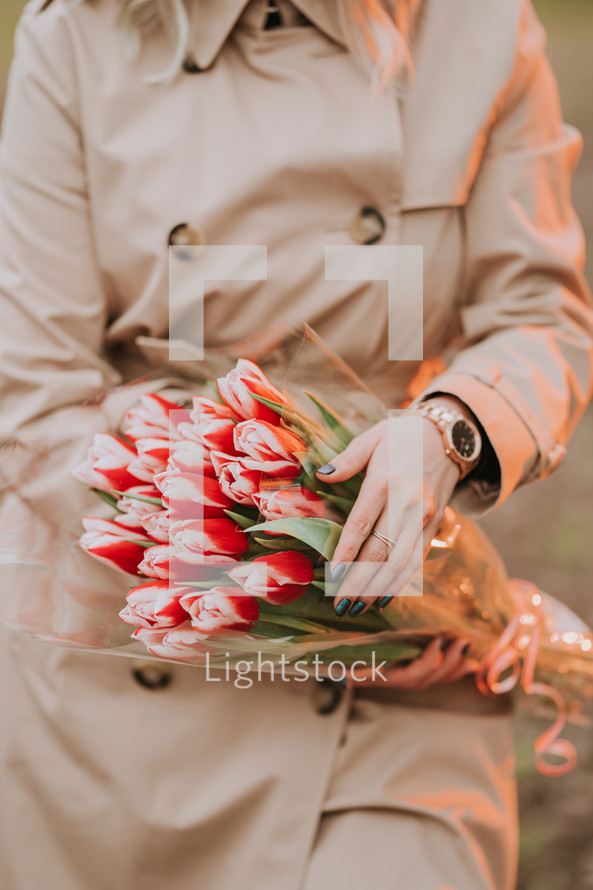 woman in classic trench coat holding bouquet of red tulips. Girl on date. International Women's Day. Congratulations concept. High quality photo