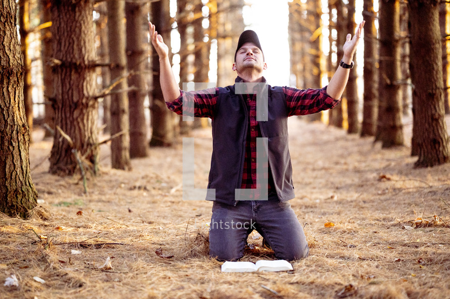 a man kneeling in a forest with hands raised 