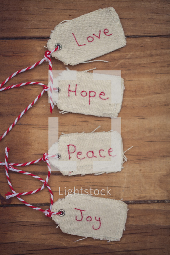 Christmas gift tags, reading "Love," "Hope," "Peace," and "Joy", on a wooden table.