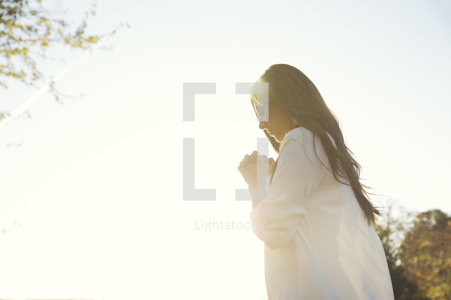 woman with praying hands outdoors under sunlight 