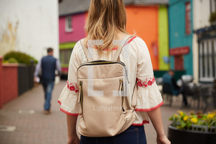 a woman walking outdoors in a harbor town with a backpack 