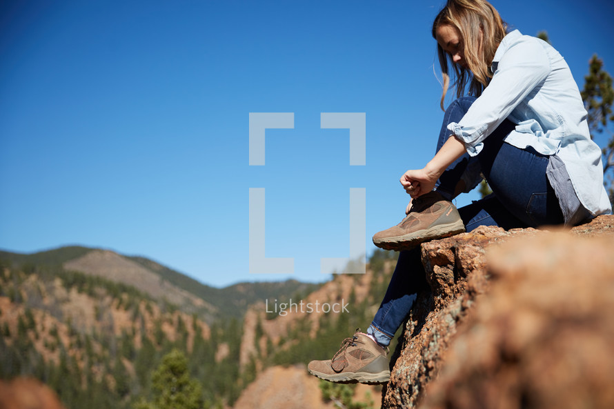 a woman sitting on a red rock on a mountainside 