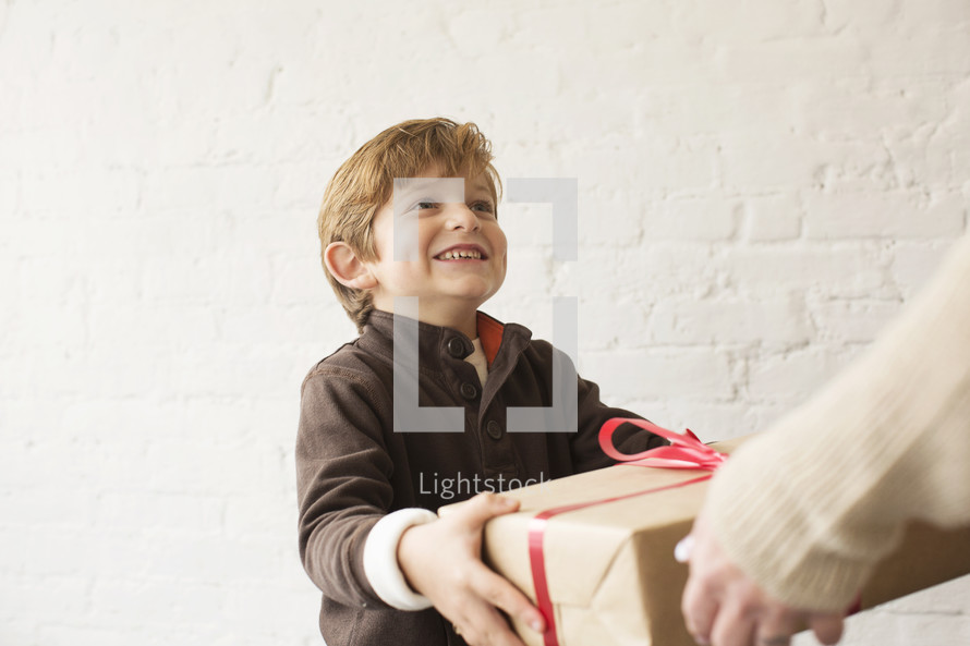 a young boy giving a wrapped gift to his mother 