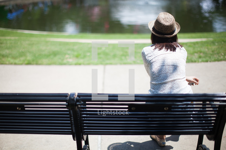 woman in a straw hat sitting on a park bench 