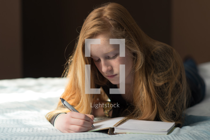 teen girl writing in a journal on a bed 