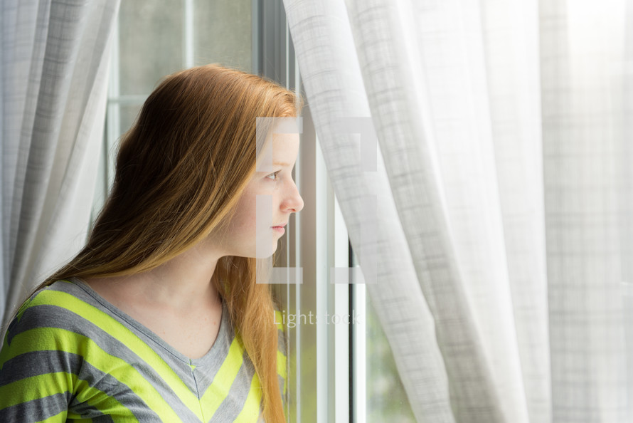 teen girl looking out a window 