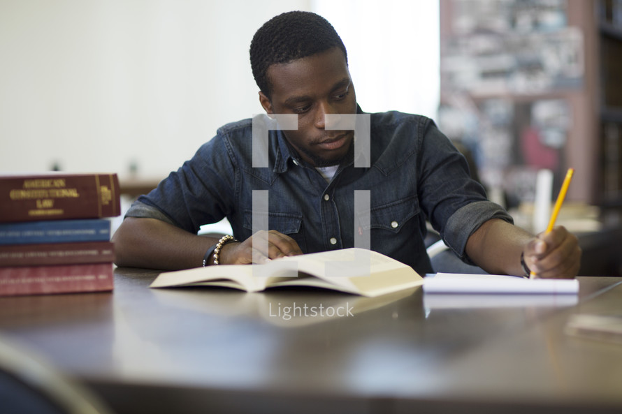 a young man taking notes at a table in a library  