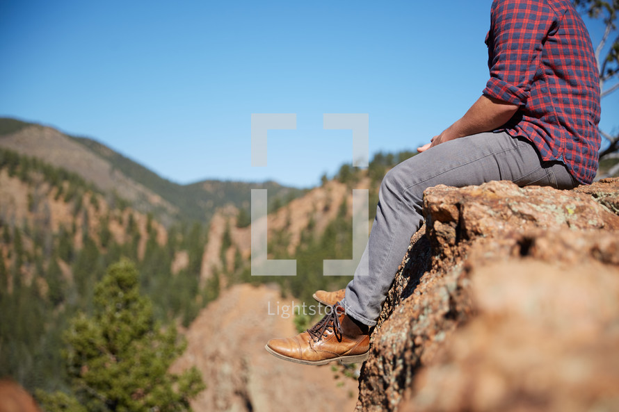 a man sitting on a rock in the mountains thinking 