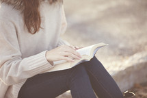 woman sitting reading a Bible outside.