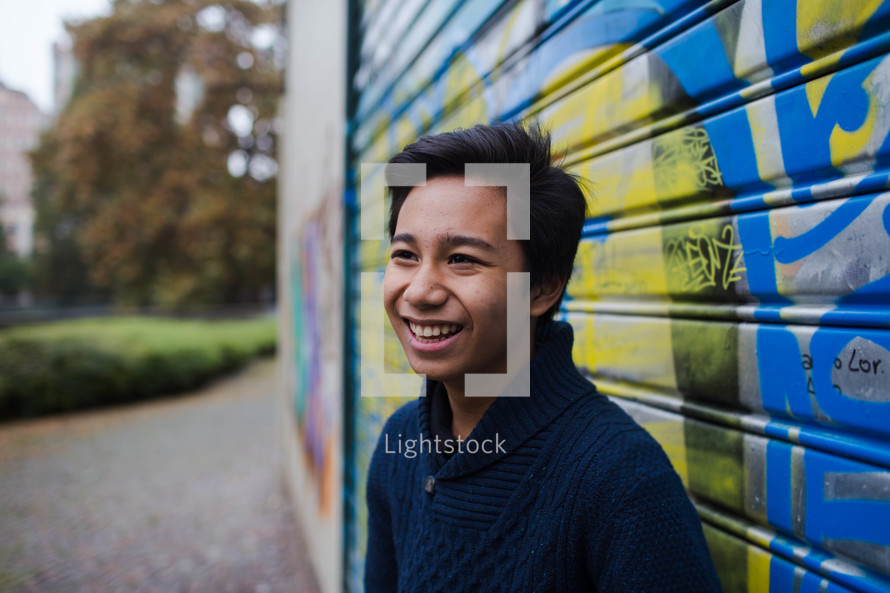 smiling teen boy in front of a graffiti covered building 