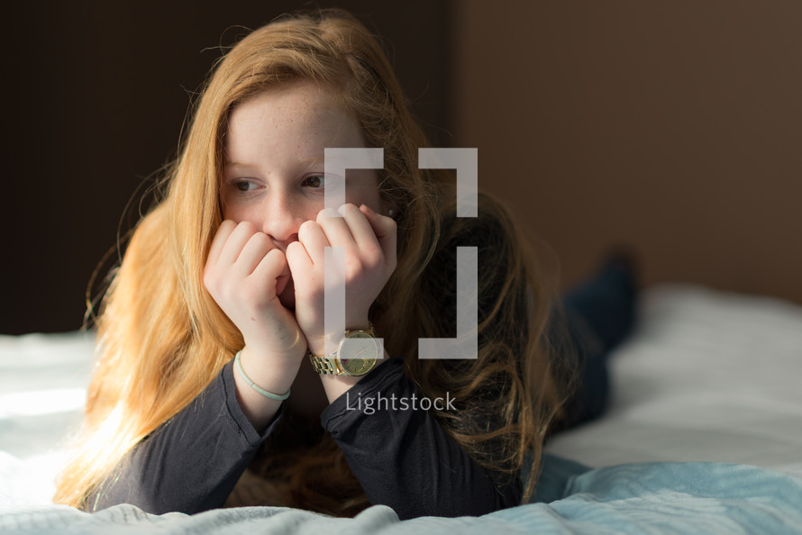 teen girl lying on a bed with her hands over her face thinking 